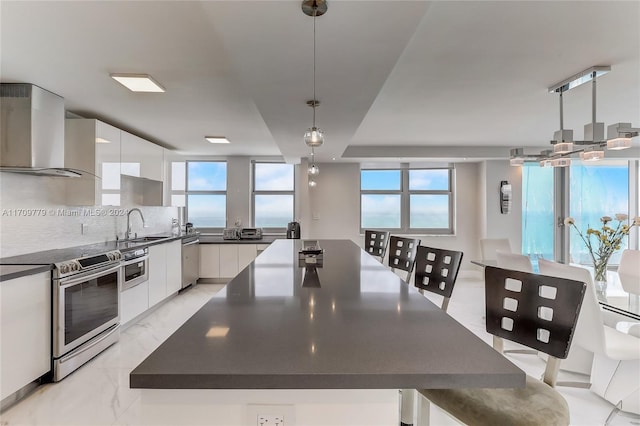 kitchen featuring decorative light fixtures, white cabinetry, stainless steel appliances, and wall chimney range hood