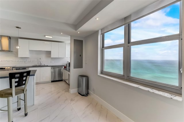 kitchen featuring wall chimney exhaust hood, white cabinetry, a water view, hanging light fixtures, and stainless steel dishwasher