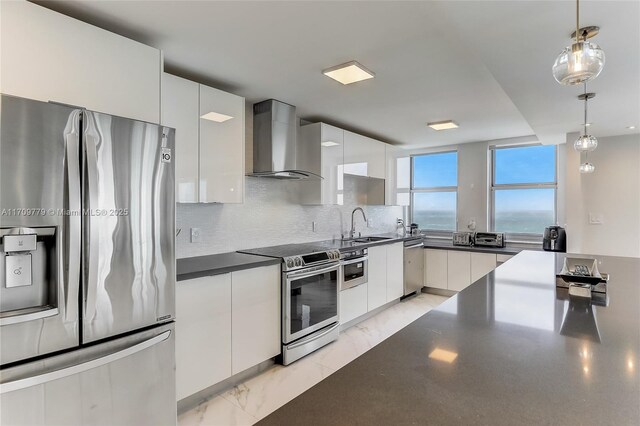 kitchen featuring dishwasher, hanging light fixtures, wall chimney range hood, white cabinets, and a water view