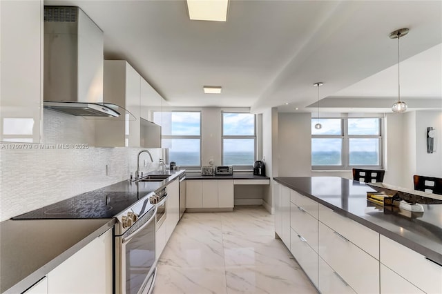 kitchen featuring wall chimney range hood, sink, white cabinets, stainless steel electric range oven, and decorative light fixtures