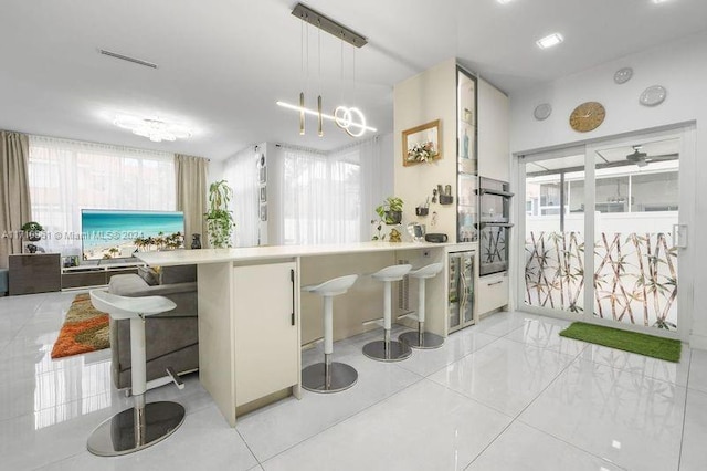 kitchen with a kitchen breakfast bar, wine cooler, kitchen peninsula, decorative light fixtures, and light tile patterned floors