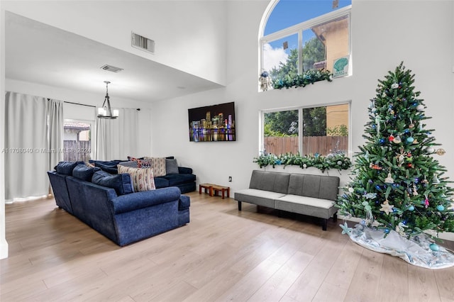 living room featuring a towering ceiling, light hardwood / wood-style floors, and an inviting chandelier