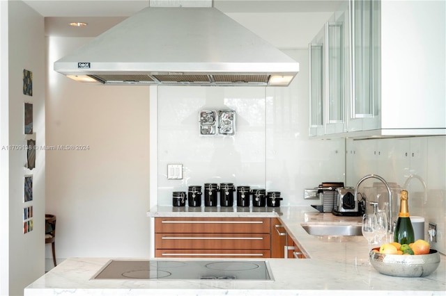 kitchen with island exhaust hood, kitchen peninsula, light stone counters, black electric cooktop, and sink