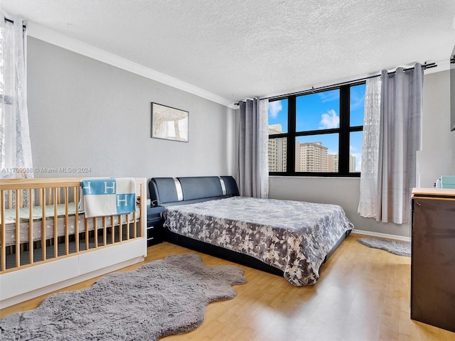 bedroom featuring a textured ceiling, light hardwood / wood-style flooring, and ornamental molding