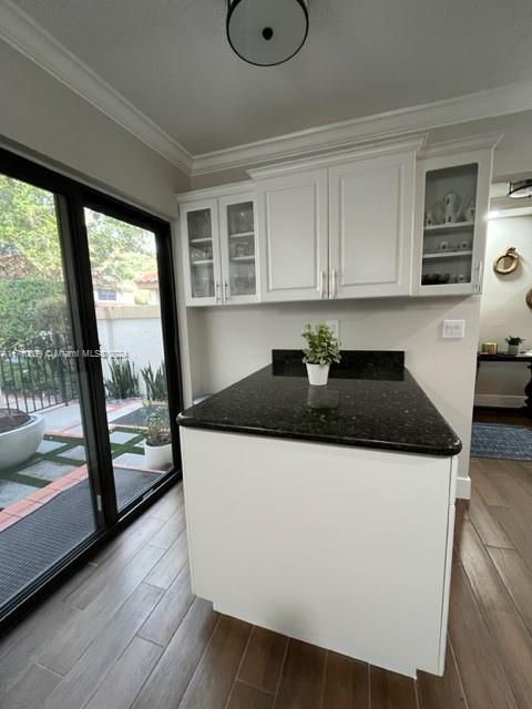 kitchen with dark stone countertops, white cabinetry, crown molding, and light hardwood / wood-style floors