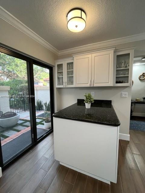 kitchen featuring dark stone counters, white cabinets, ornamental molding, a textured ceiling, and dark hardwood / wood-style flooring