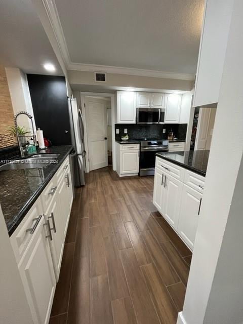 kitchen featuring sink, dark wood-type flooring, stainless steel appliances, dark stone countertops, and white cabinets