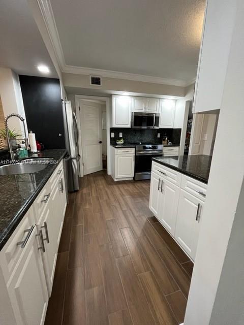 kitchen featuring sink, stainless steel appliances, dark hardwood / wood-style floors, dark stone counters, and white cabinets