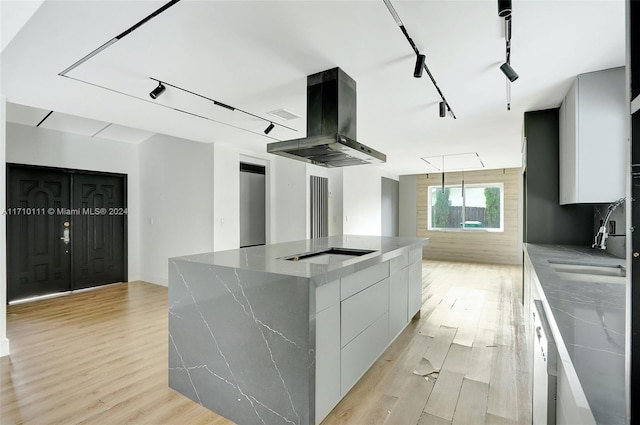 kitchen featuring a large island, ventilation hood, light hardwood / wood-style floors, black stovetop, and white cabinets