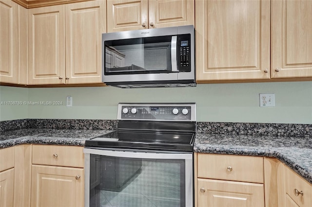 kitchen with light brown cabinets, stainless steel appliances, and dark stone countertops