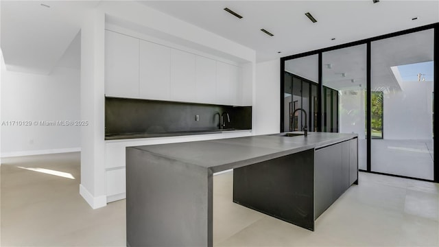 kitchen featuring white cabinets, a center island with sink, a wall of windows, and sink