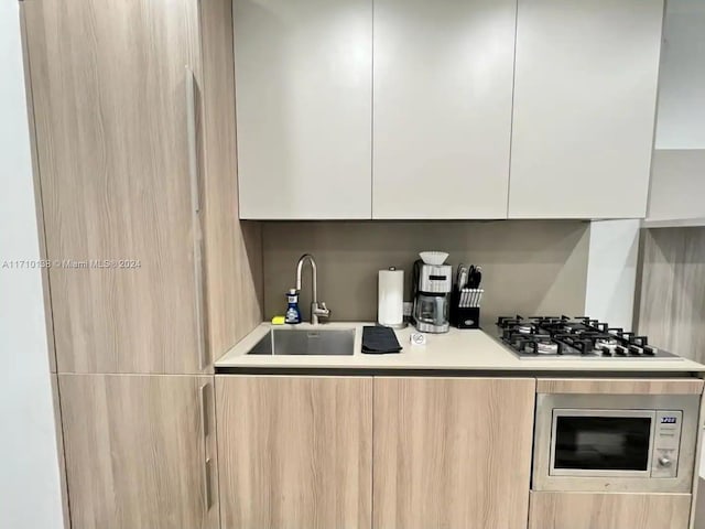 kitchen featuring white cabinets, light brown cabinets, stainless steel microwave, and sink