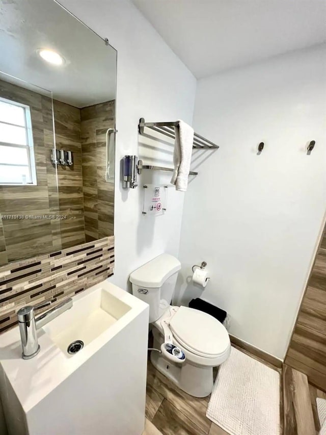 bathroom featuring tasteful backsplash, sink, tiled shower, wood-type flooring, and toilet