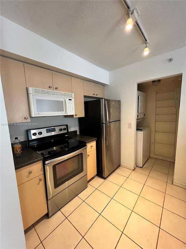 kitchen featuring track lighting, a textured ceiling, stainless steel appliances, light tile patterned floors, and stacked washer / drying machine