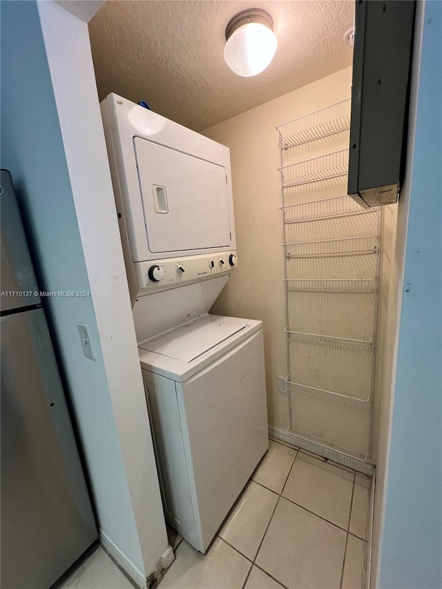 washroom with light tile patterned floors, a textured ceiling, electric panel, and stacked washer / dryer