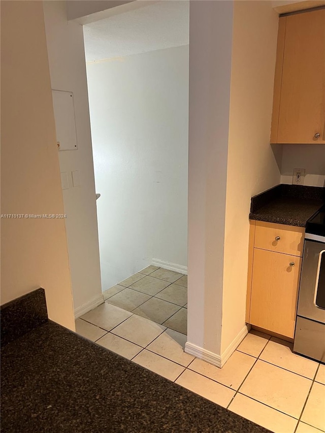 kitchen with light brown cabinets, light tile patterned floors, and stainless steel electric range