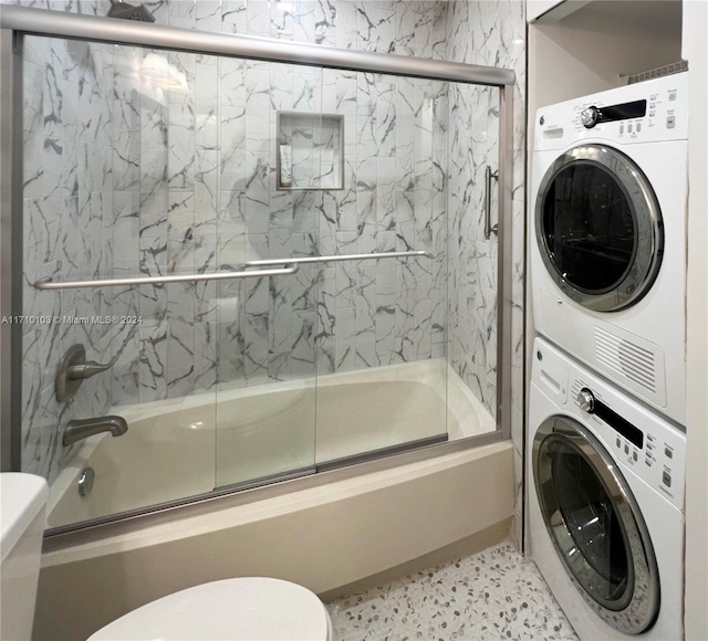 bathroom featuring toilet, enclosed tub / shower combo, and stacked washer and clothes dryer