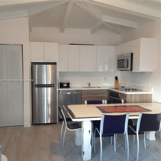 kitchen featuring kitchen peninsula, appliances with stainless steel finishes, a breakfast bar, white cabinets, and vaulted ceiling with beams