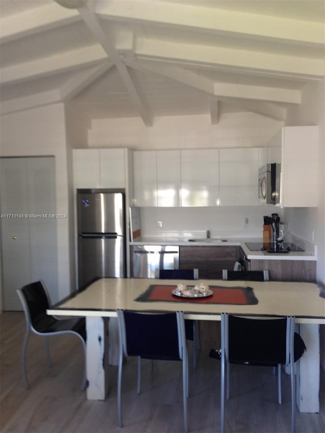 kitchen featuring appliances with stainless steel finishes, a breakfast bar, lofted ceiling with beams, hardwood / wood-style floors, and white cabinetry