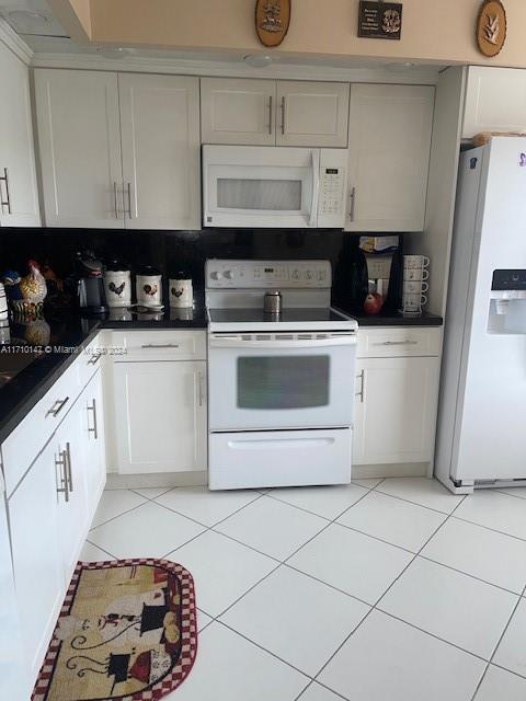 kitchen featuring white cabinetry, light tile patterned flooring, white appliances, and tasteful backsplash