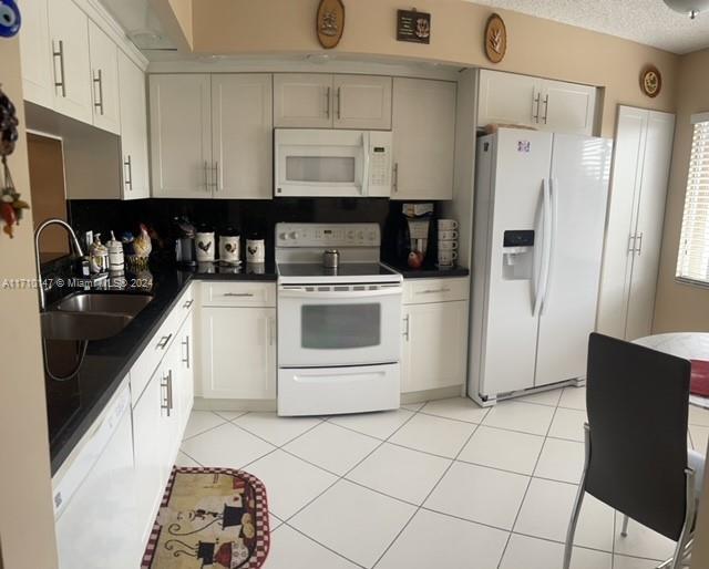 kitchen with white cabinetry, white appliances, sink, and light tile patterned floors