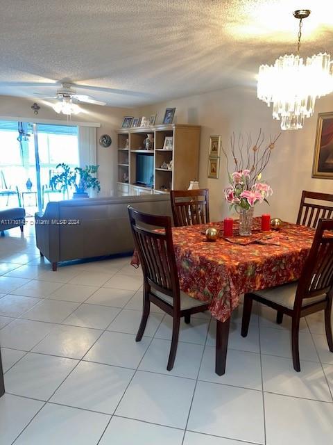 tiled dining room featuring ceiling fan with notable chandelier and a textured ceiling