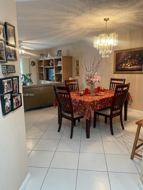 tiled dining area with ceiling fan with notable chandelier and a textured ceiling