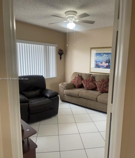 living room featuring ceiling fan, light tile patterned flooring, and a textured ceiling