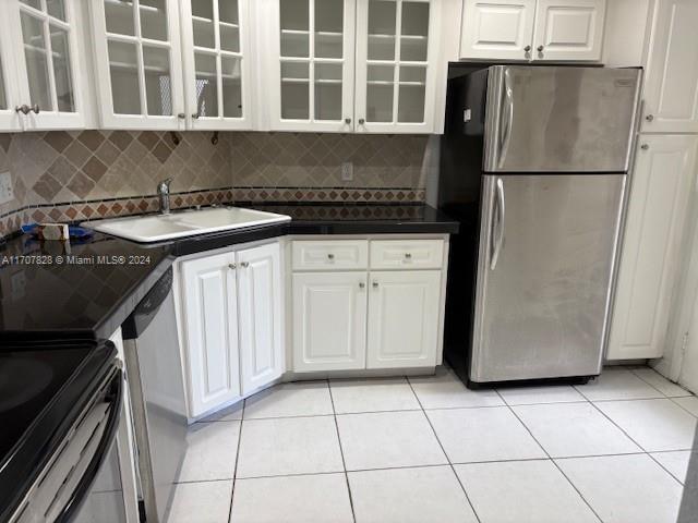 kitchen with appliances with stainless steel finishes, light tile patterned floors, white cabinetry, and sink