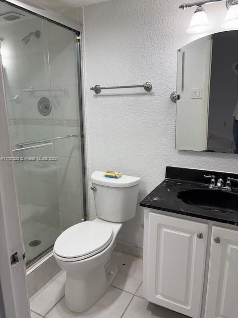 bathroom featuring tile patterned floors, vanity, an enclosed shower, and toilet