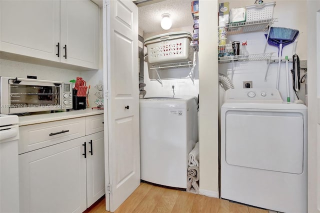 clothes washing area with a textured ceiling, light hardwood / wood-style floors, and washing machine and clothes dryer