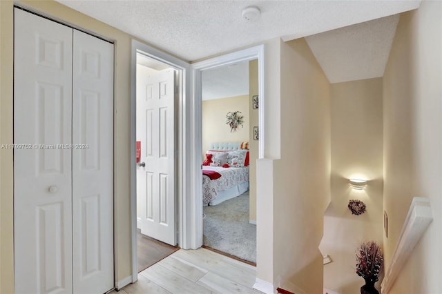 hallway with a textured ceiling and light hardwood / wood-style flooring