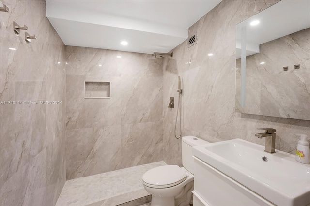 bathroom featuring tiled shower, vanity, tile walls, and toilet