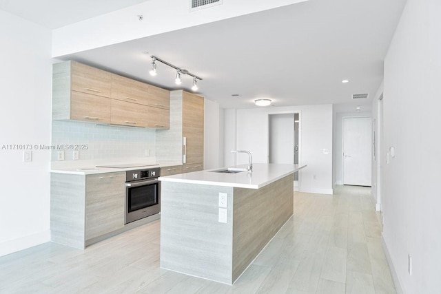 kitchen with a center island with sink, black electric cooktop, tasteful backsplash, oven, and sink