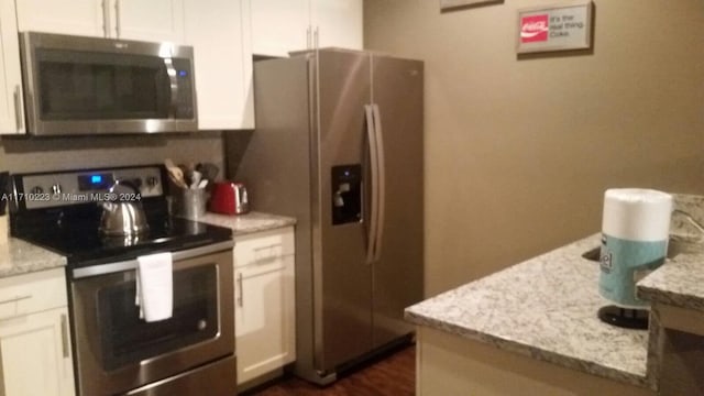 kitchen with light stone countertops, stainless steel appliances, white cabinetry, and dark wood-type flooring