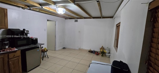 basement featuring stainless steel fridge and light tile patterned flooring