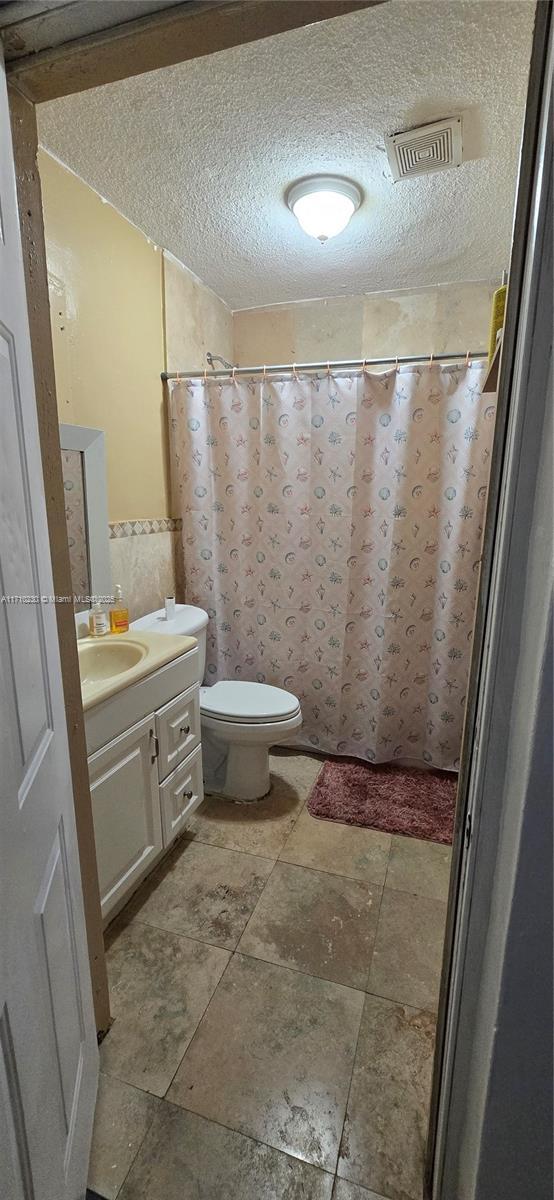 bathroom featuring toilet, vanity, walk in shower, and a textured ceiling