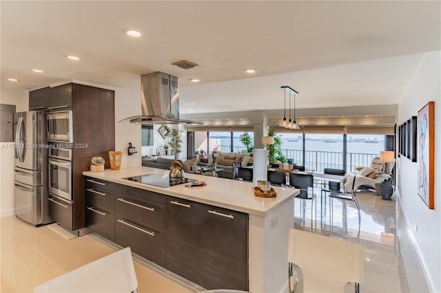 kitchen with appliances with stainless steel finishes, dark brown cabinets, island range hood, light tile patterned floors, and pendant lighting