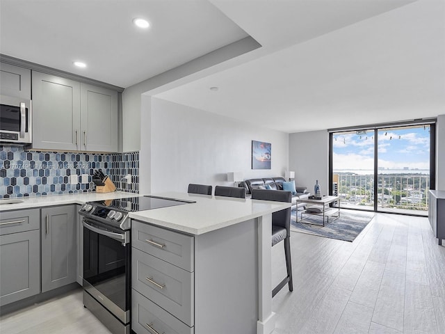 kitchen featuring gray cabinetry, stainless steel appliances, backsplash, light hardwood / wood-style floors, and a breakfast bar