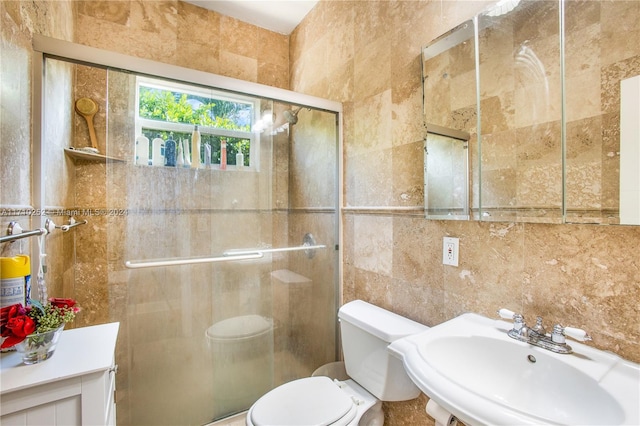 bathroom featuring toilet, sink, a shower with shower door, and tile walls