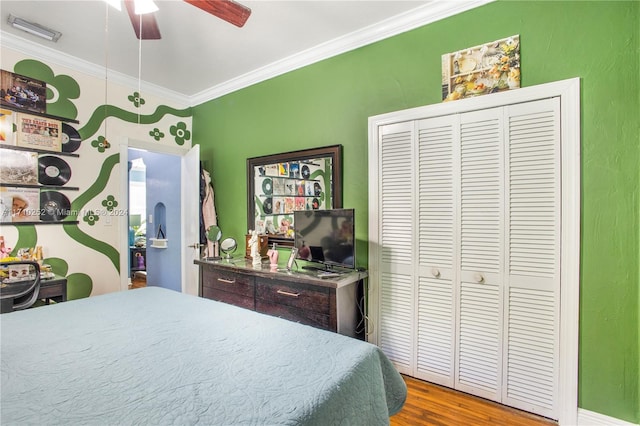 bedroom featuring ceiling fan, wood-type flooring, ornamental molding, and a closet