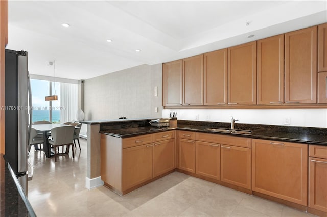 kitchen featuring a peninsula, dark stone counters, a sink, freestanding refrigerator, and expansive windows