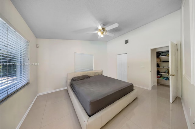 bedroom with a textured ceiling, ceiling fan, light tile patterned floors, a closet, and lofted ceiling