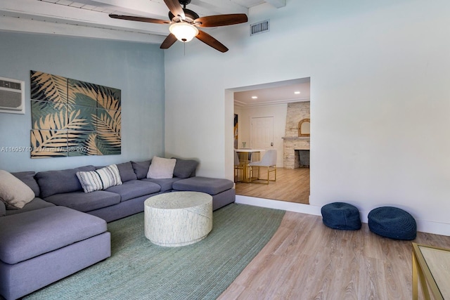 living room featuring ceiling fan, a wall mounted AC, hardwood / wood-style floors, a fireplace, and ornamental molding