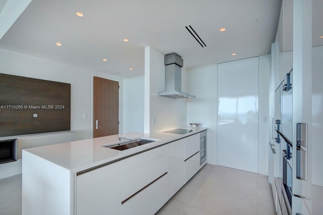 kitchen featuring kitchen peninsula, white oven, sink, wall chimney range hood, and white cabinetry