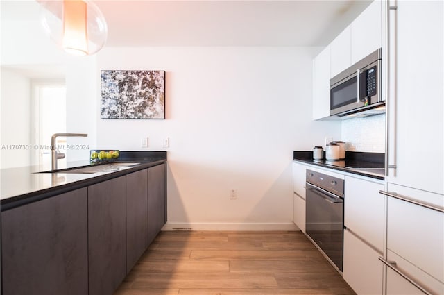 kitchen featuring white cabinets, sink, light wood-type flooring, tasteful backsplash, and stainless steel appliances