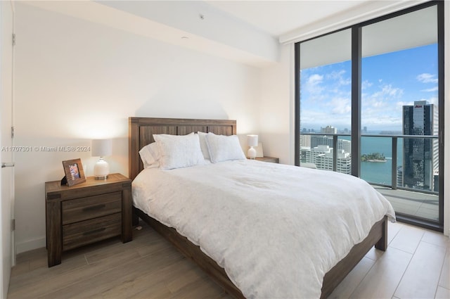 bedroom featuring access to exterior, a water view, light hardwood / wood-style flooring, and floor to ceiling windows