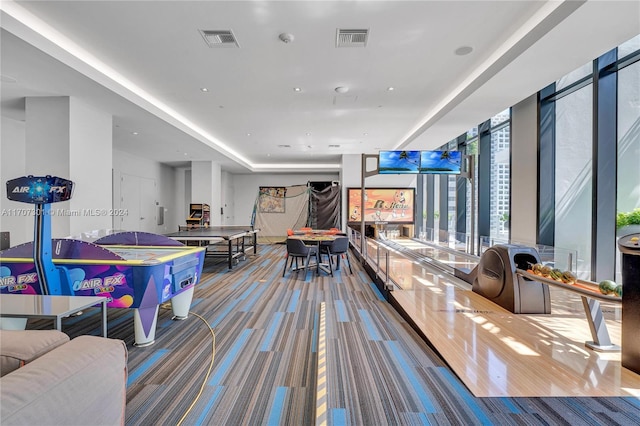 recreation room with bowling, carpet floors, a raised ceiling, and a wall of windows