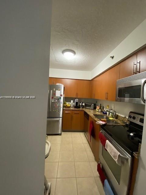 kitchen featuring appliances with stainless steel finishes, sink, light tile patterned floors, and a textured ceiling