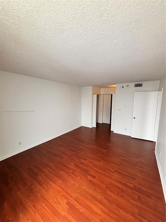 spare room with a textured ceiling and dark hardwood / wood-style flooring